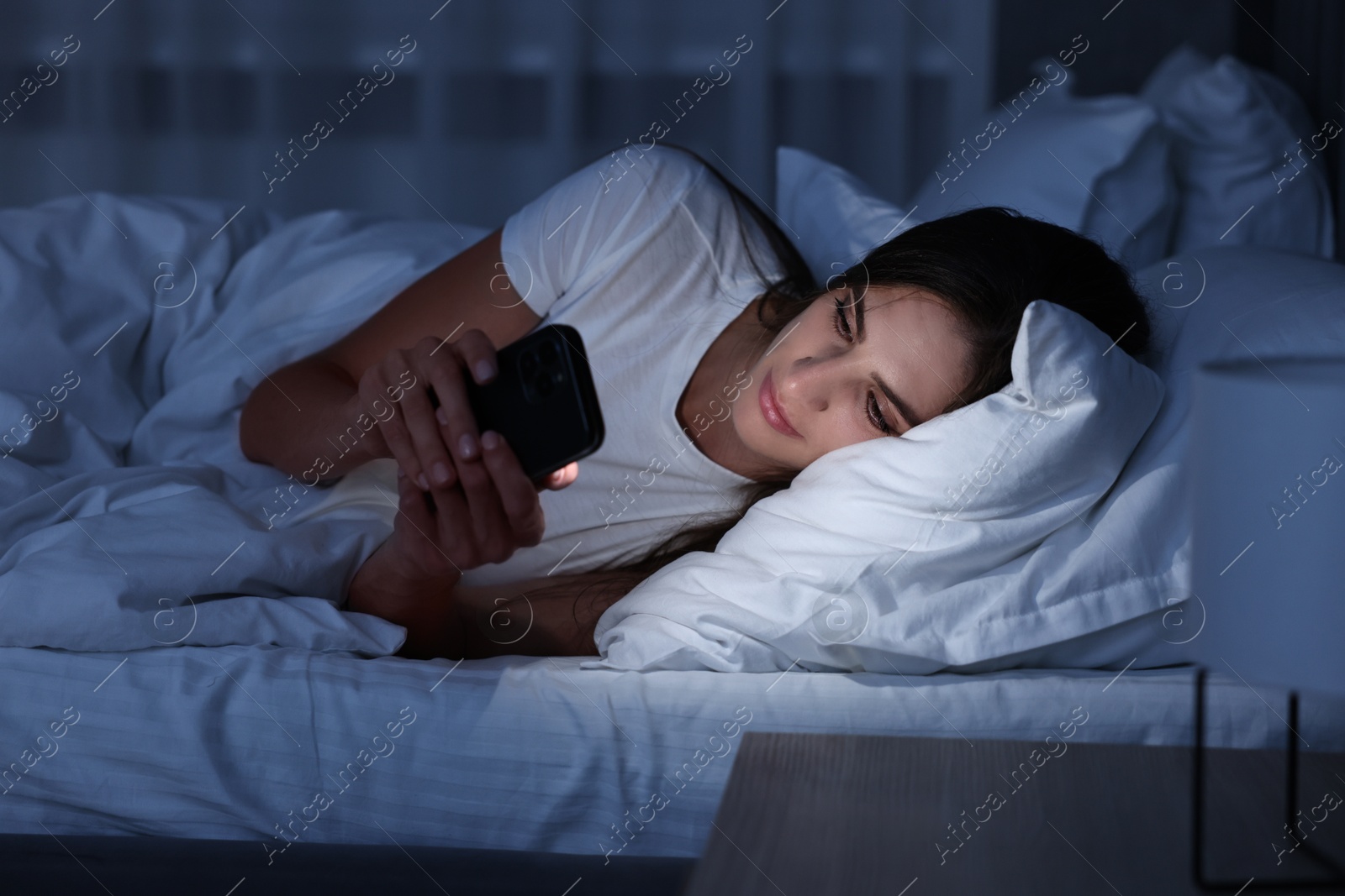 Photo of Bad habit. Young woman using smartphone in bed at night