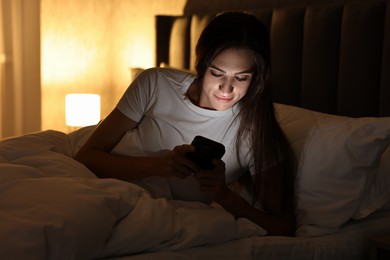 Photo of Bad habit. Young woman using smartphone in bed at night