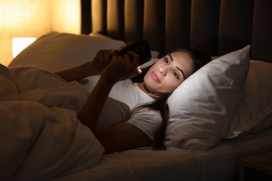 Photo of Bad habit. Young woman using smartphone in bed at night