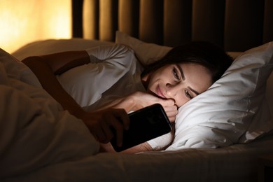 Photo of Bad habit. Young woman using smartphone in bed at night