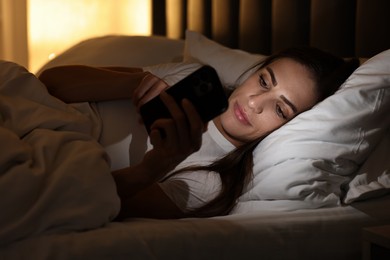 Photo of Bad habit. Young woman using smartphone in bed at night