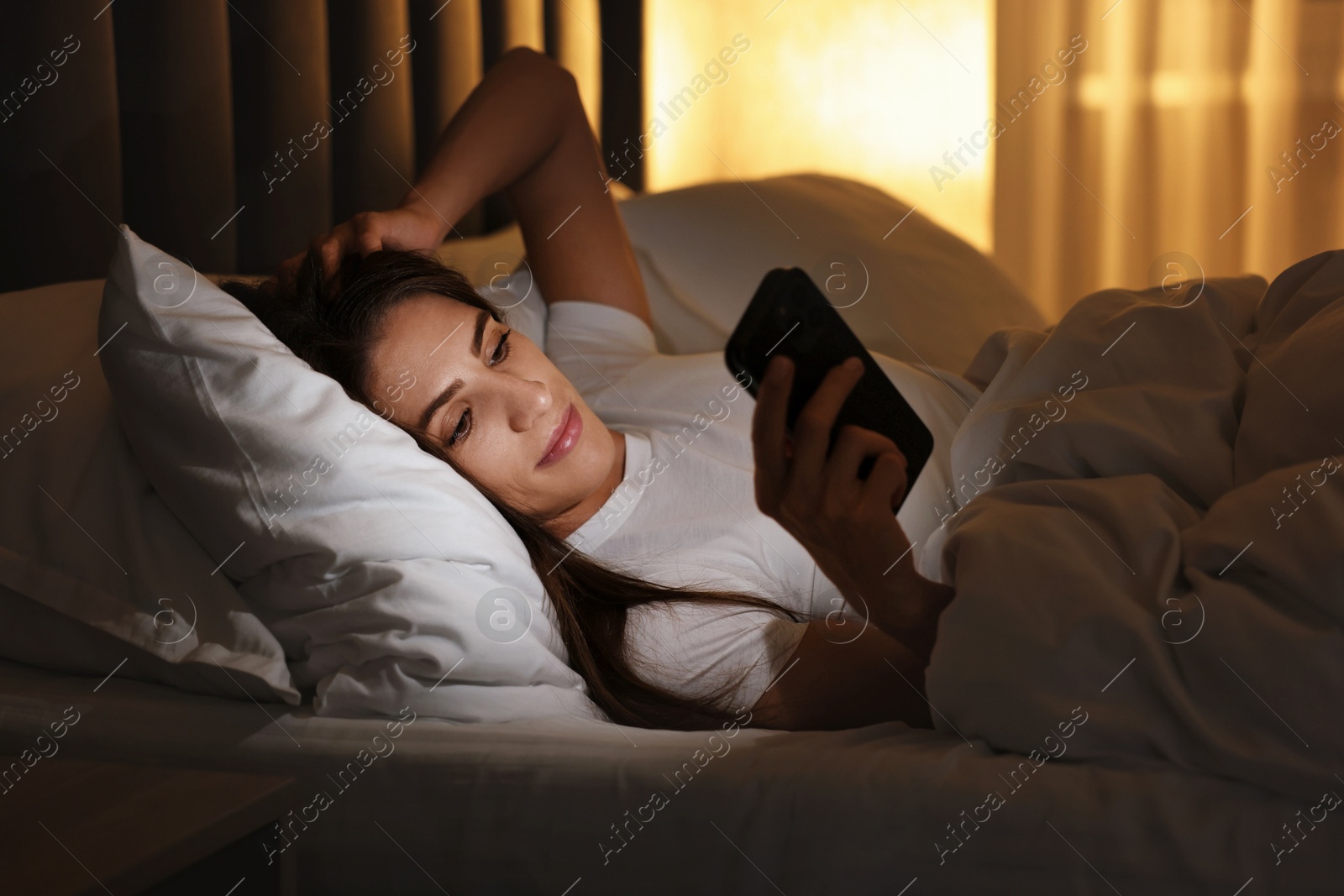 Photo of Bad habit. Young woman using smartphone in bed at night