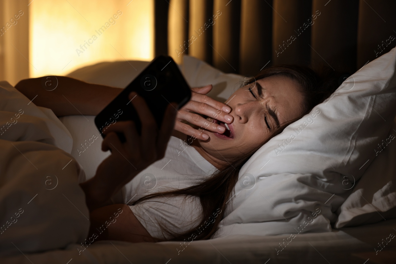 Photo of Bad habit. Young woman using smartphone in bed at night