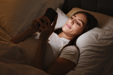 Photo of Bad habit. Young woman using smartphone in bed at night