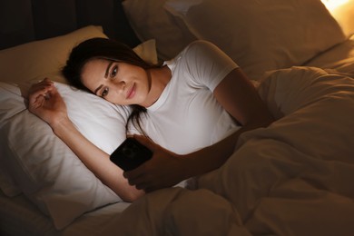 Photo of Bad habit. Young woman using smartphone in bed at night