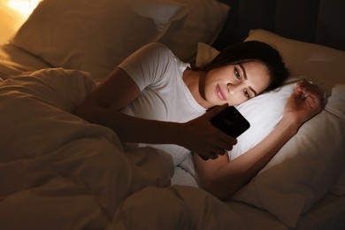 Photo of Bad habit. Young woman using smartphone in bed at night