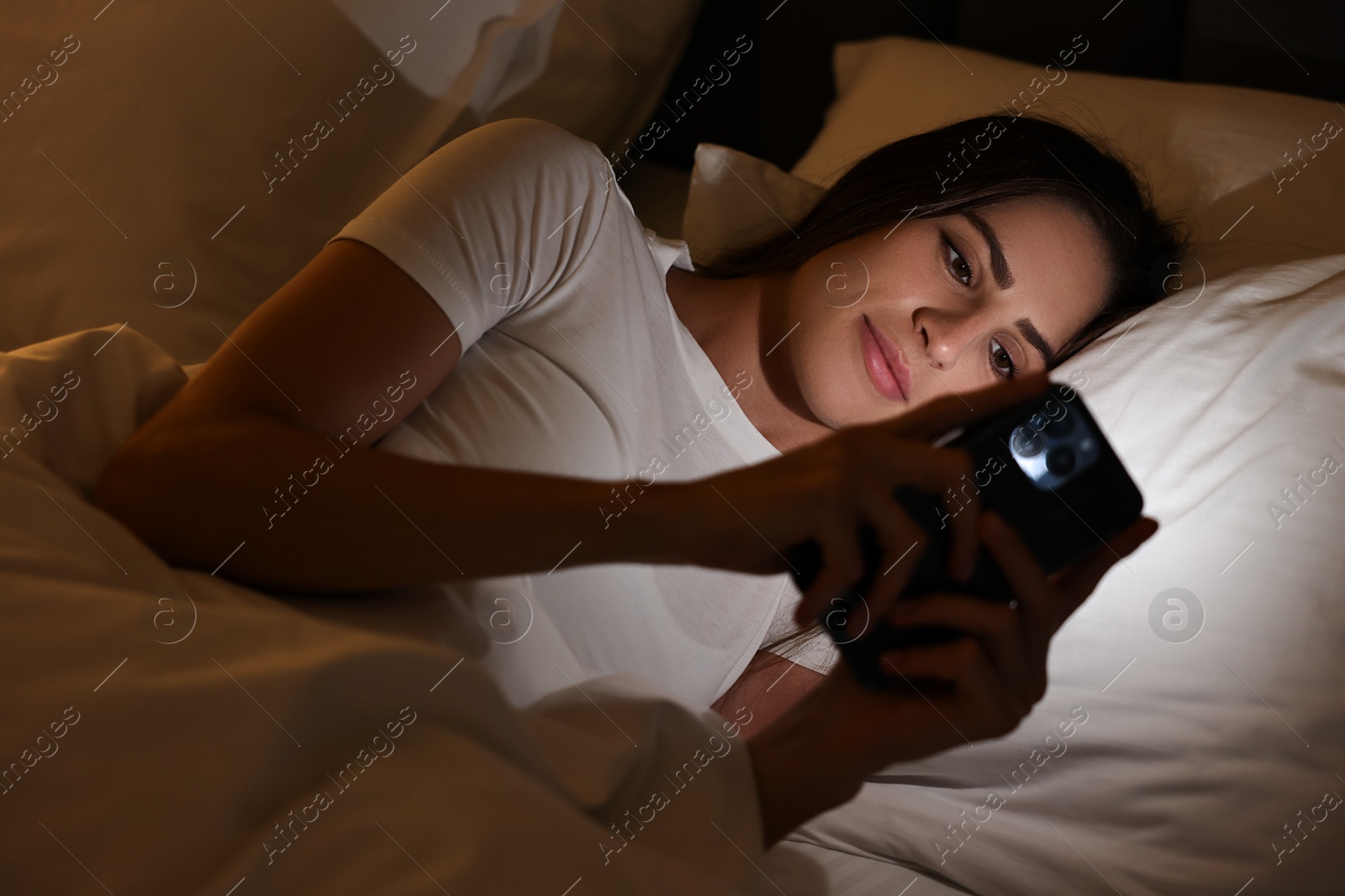 Photo of Bad habit. Young woman using smartphone in bed at night