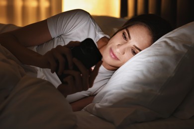 Photo of Bad habit. Young woman using smartphone in bed at night