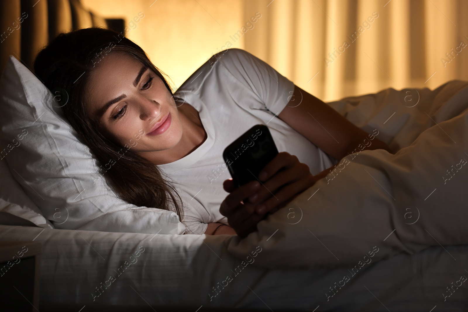 Photo of Bad habit. Young woman using smartphone in bed at night