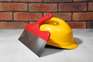 Hard hat and plastering trowel on light textured table against red brick wall