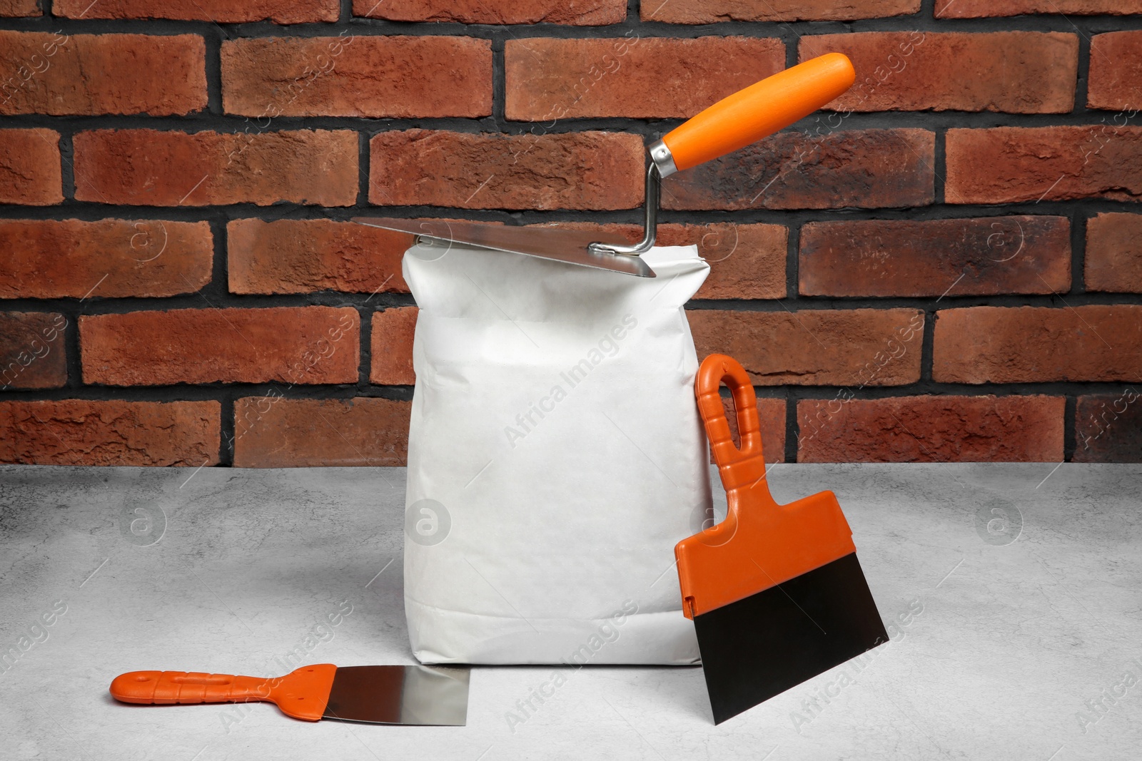 Photo of Bag of cement and trowels on light textured table against red brick wall