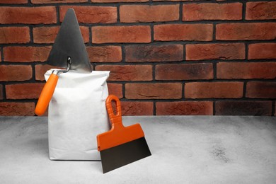 Photo of Bag of cement and trowels on light textured table against red brick wall. Space for text