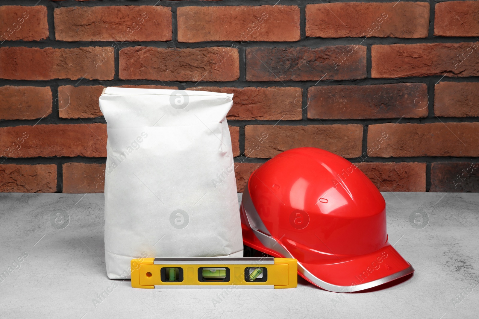 Photo of Bag of cement and construction tools on light textured table against red brick wall