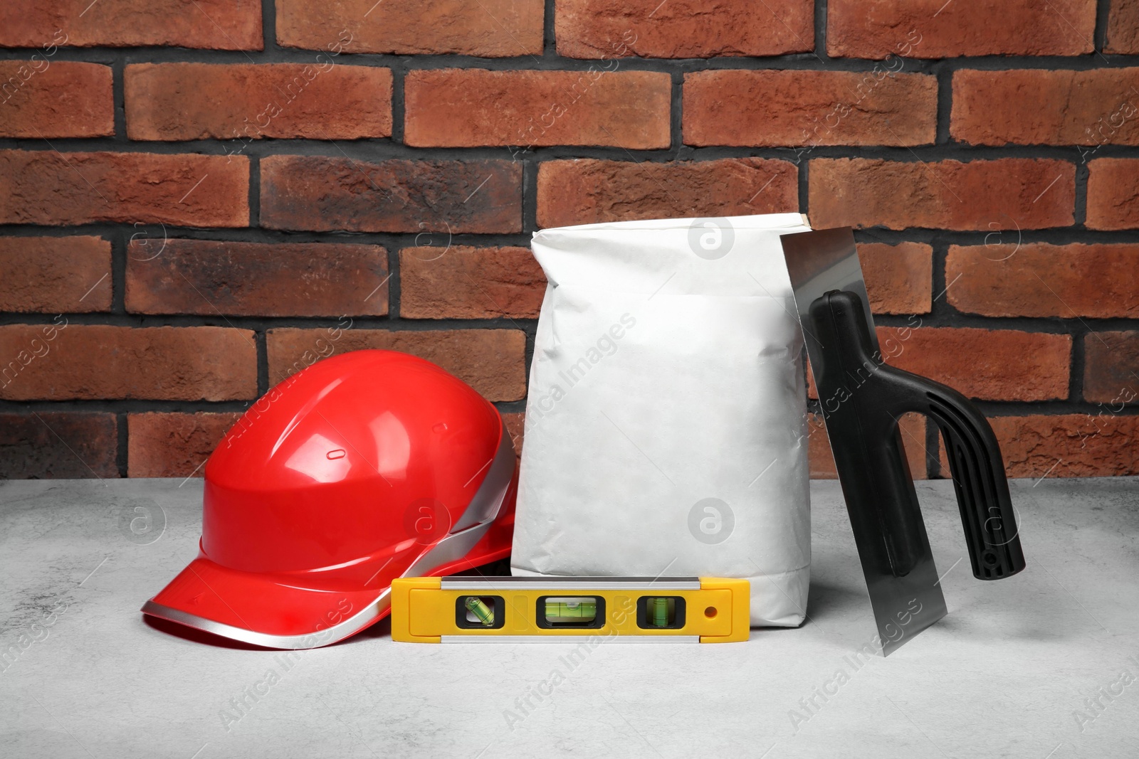 Photo of Bag of cement and construction tools on light textured table against red brick wall