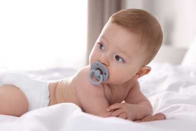 Cute little baby with pacifier on bed at home