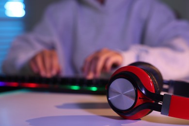 Photo of Woman playing video game with keyboard and headphones at table indoors, selective focus