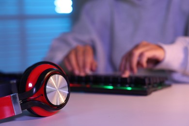 Woman playing video game with keyboard and headphones at table indoors, selective focus