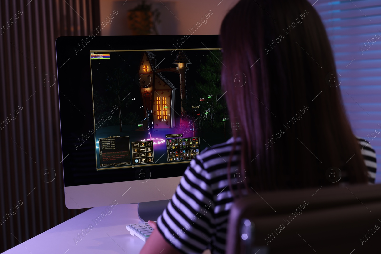 Photo of Woman playing video game with keyboard at table indoors, back view