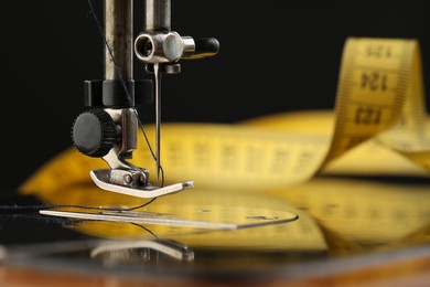 Photo of Professional sewing machine and measuring tape on black background, macro view