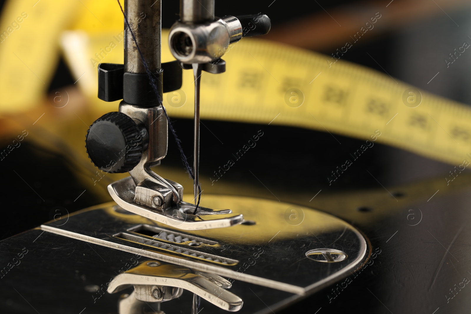 Photo of Professional sewing machine and measuring tape on blurred background, macro view