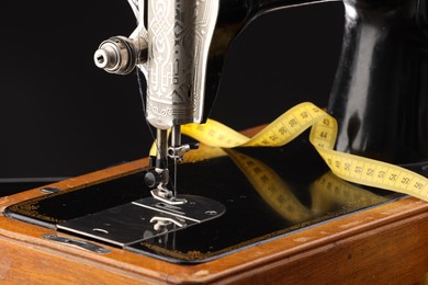 Photo of Professional sewing machine and measuring tape on black background, closeup