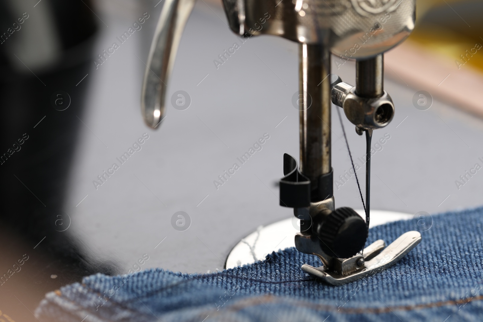 Photo of Professional sewing machine with denim fabric on blurred background, macro view