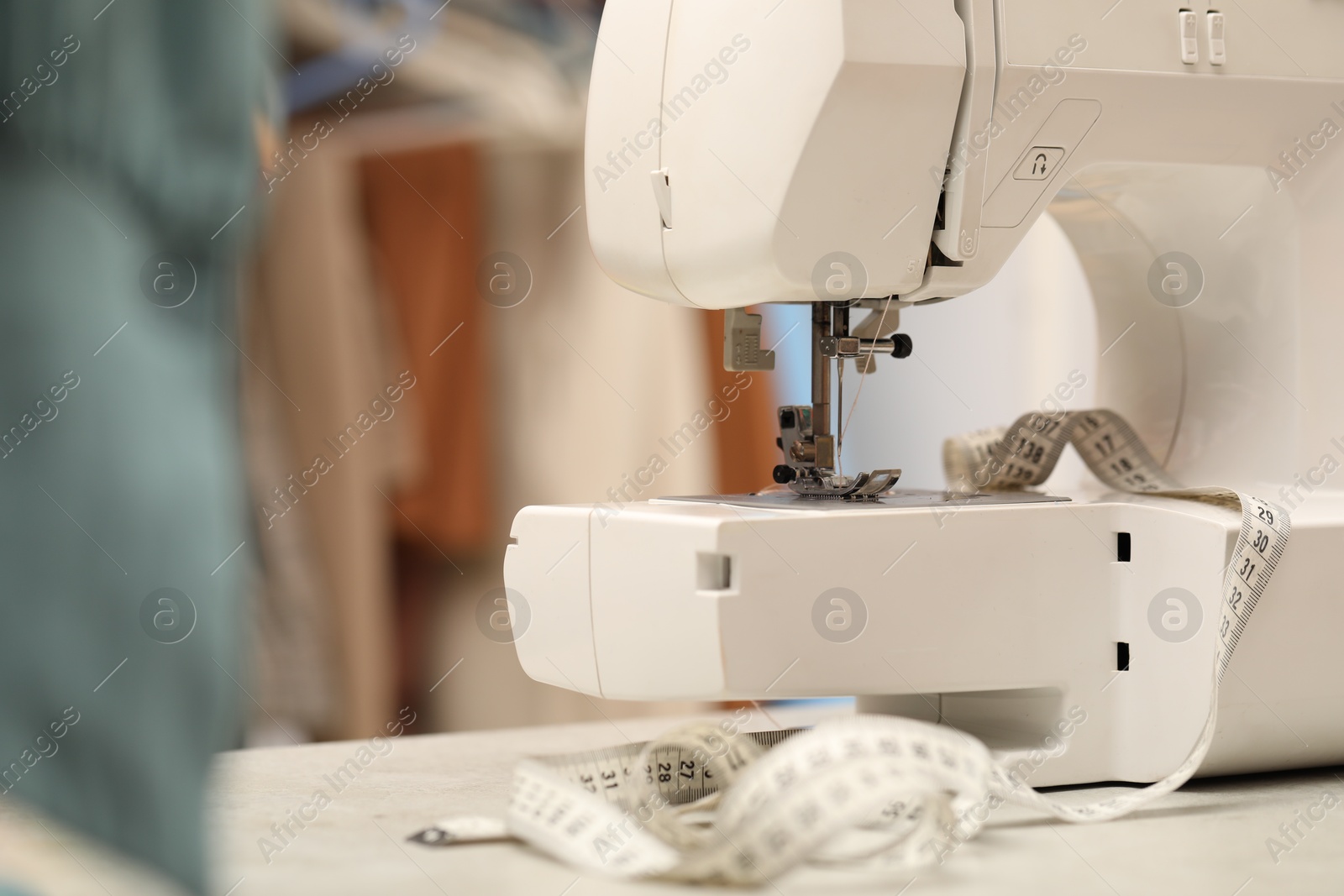 Photo of One sewing machine with thread and measuring tape on white table in workshop