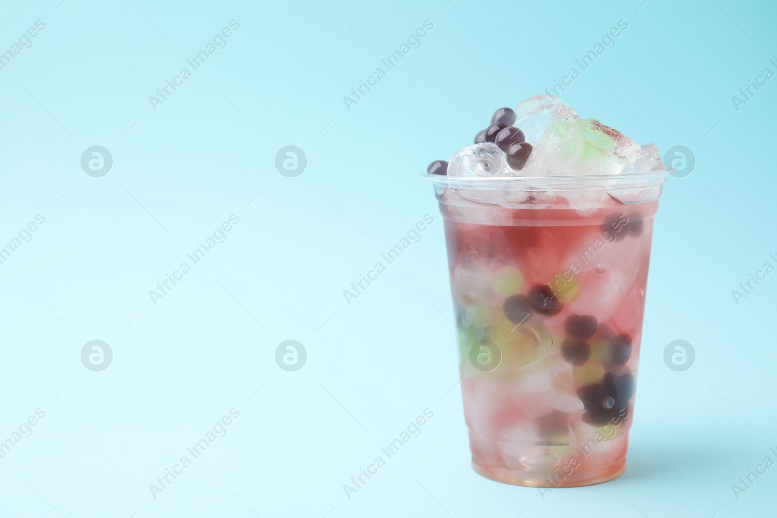 Photo of Tasty bubble tea in plastic cup on light blue background, space for text