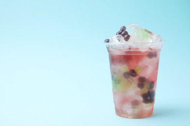 Photo of Tasty bubble tea in plastic cup on light blue background, space for text