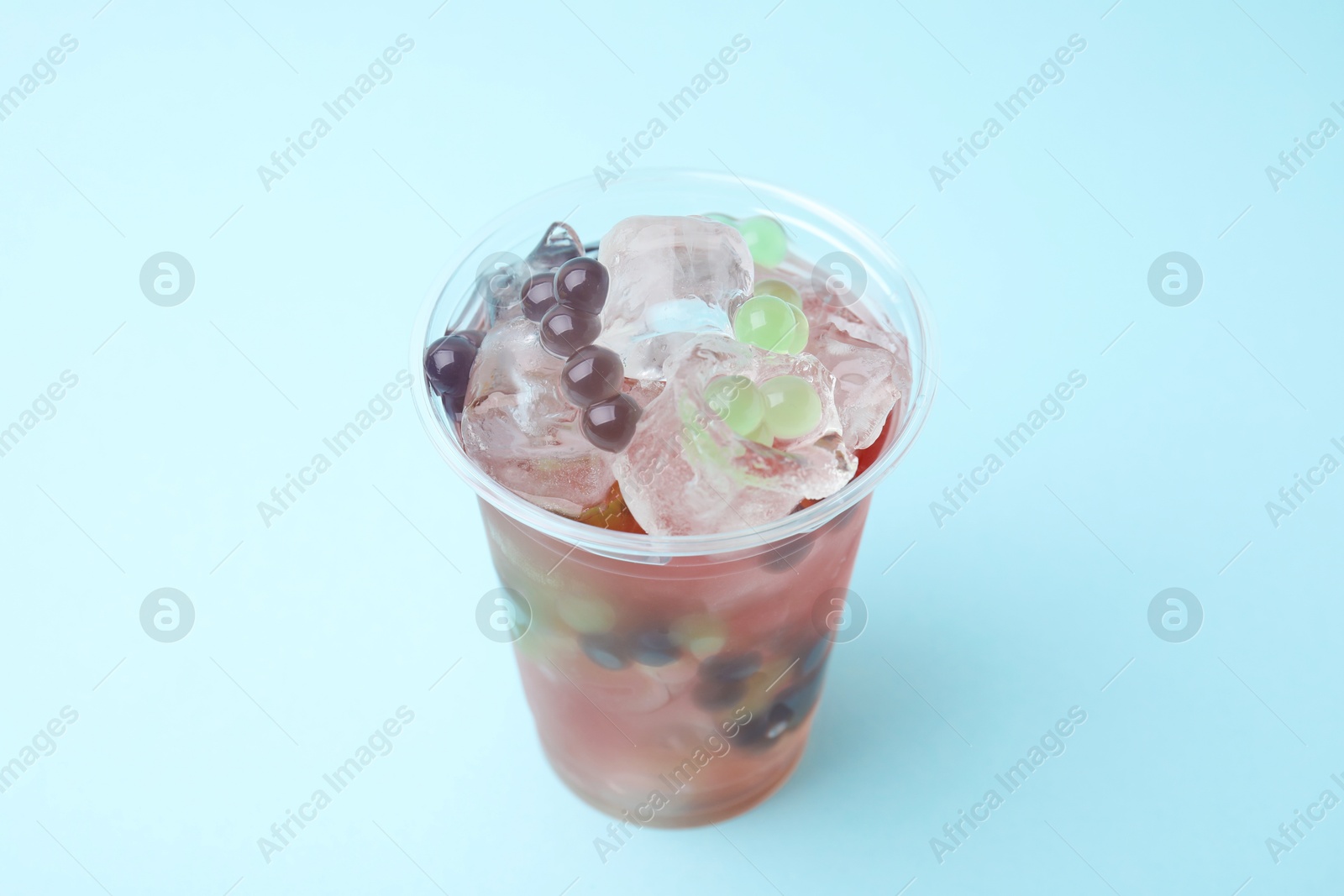 Photo of Tasty bubble tea in plastic cup on light blue background