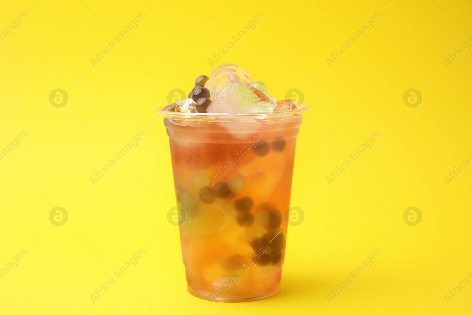 Photo of Tasty bubble tea in plastic cup on yellow background