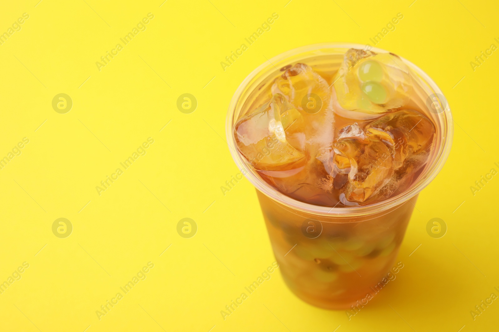 Photo of Tasty bubble tea in plastic cup on yellow background, closeup. Space for text