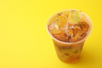 Photo of Tasty bubble tea in plastic cup on yellow background, closeup. Space for text