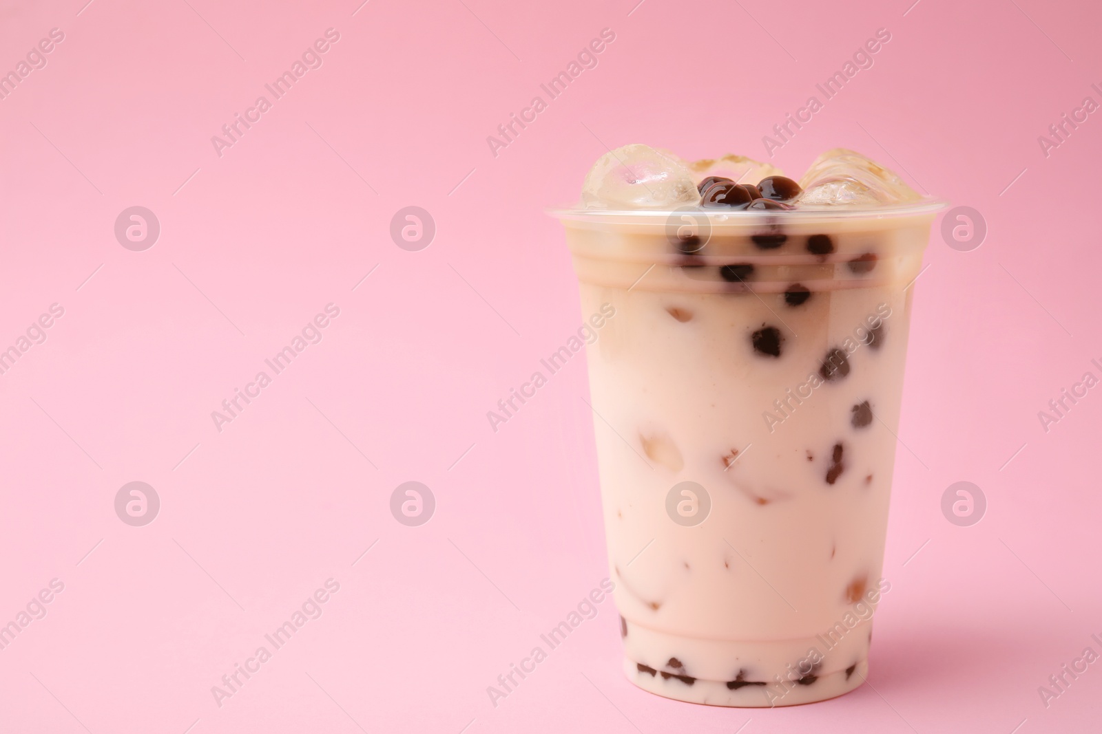 Photo of Tasty milk bubble tea in plastic cup on pink background, space for text