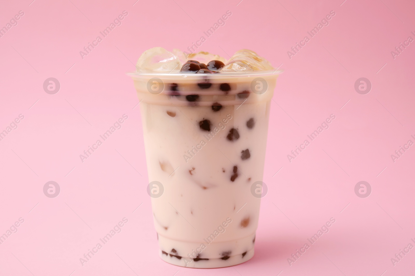 Photo of Tasty milk bubble tea in plastic cup on pink background