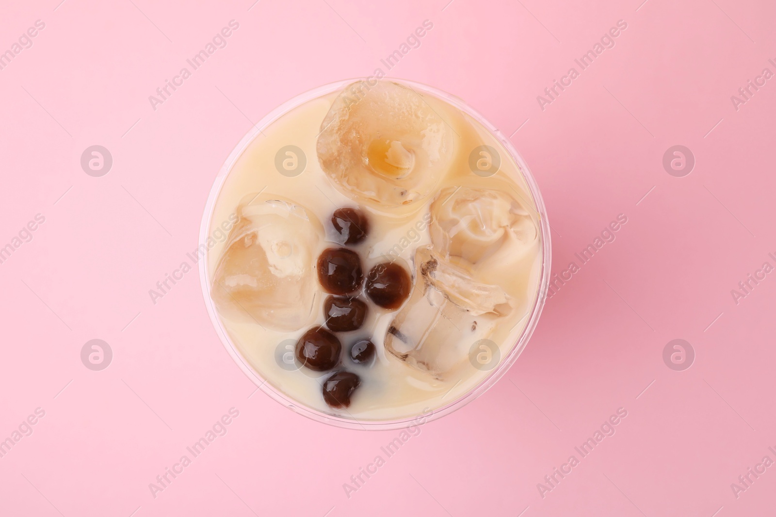 Photo of Tasty milk bubble tea in plastic cup on pink background, top view