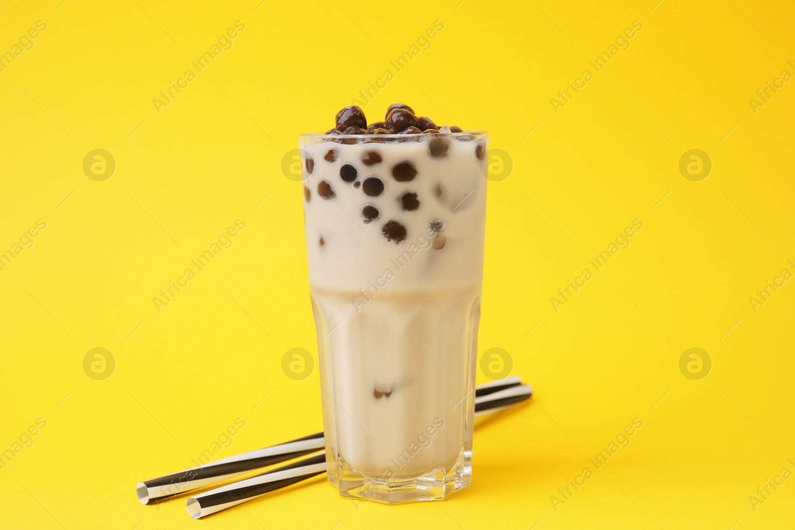 Photo of Tasty milk bubble tea in glass and straws on yellow background