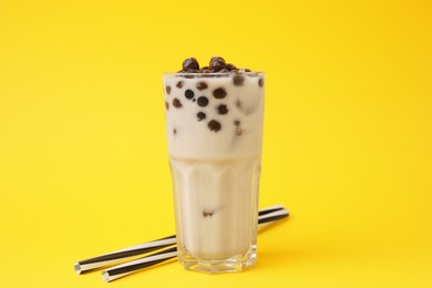 Photo of Tasty milk bubble tea in glass and straws on yellow background