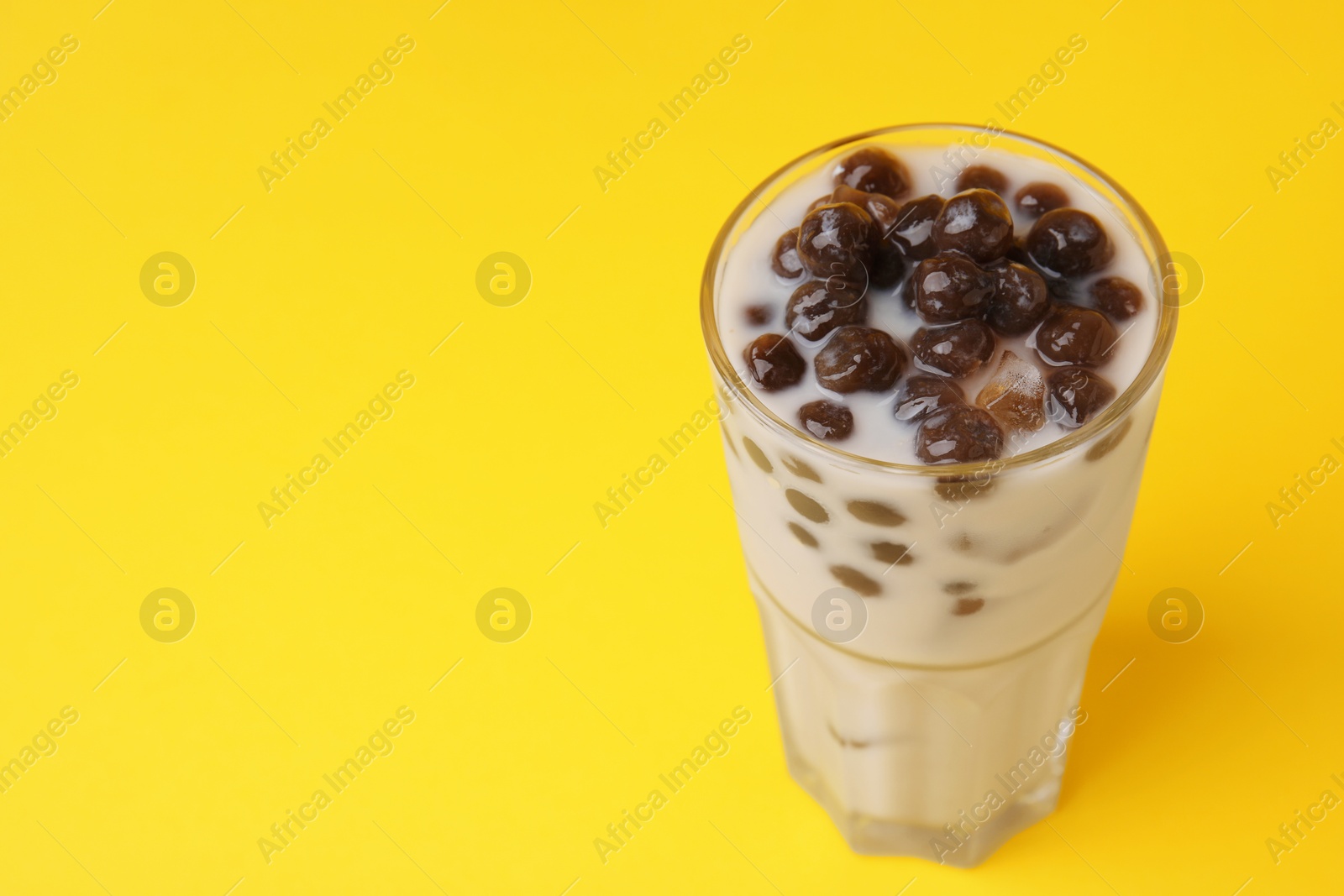 Photo of Tasty milk bubble tea in glass on yellow background, closeup. Space for text