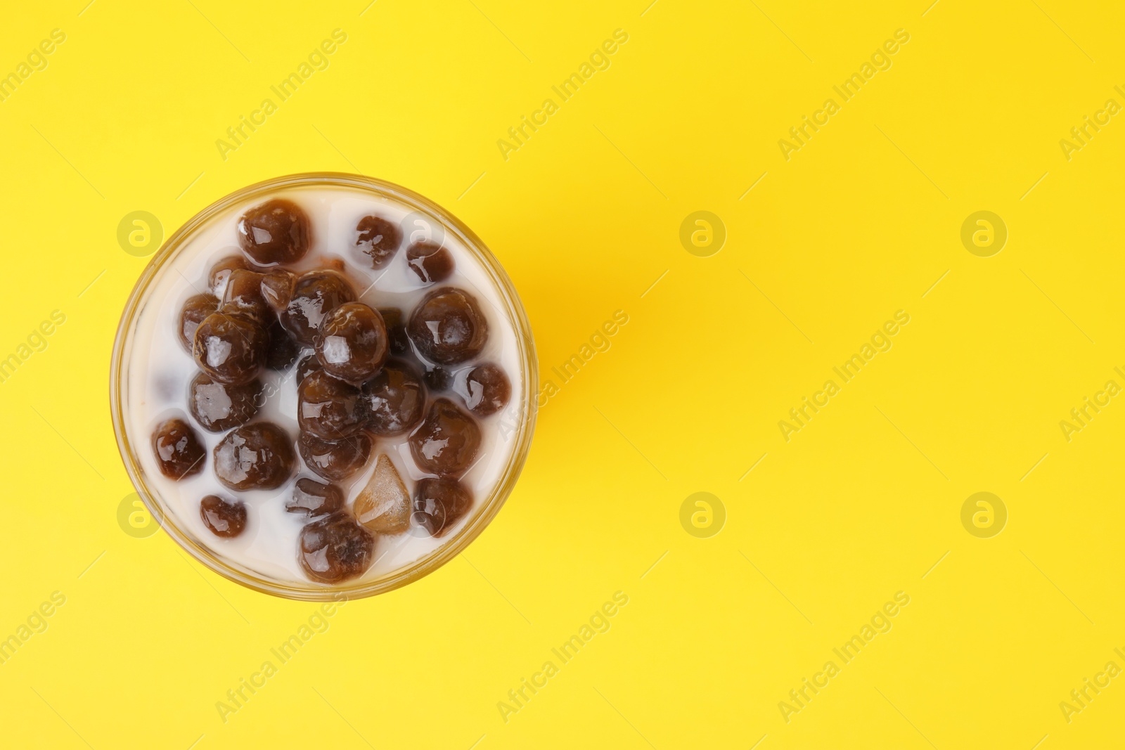 Photo of Tasty milk bubble tea in glass on yellow background, top view. Space for text