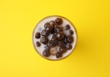 Photo of Tasty milk bubble tea in glass on yellow background, top view