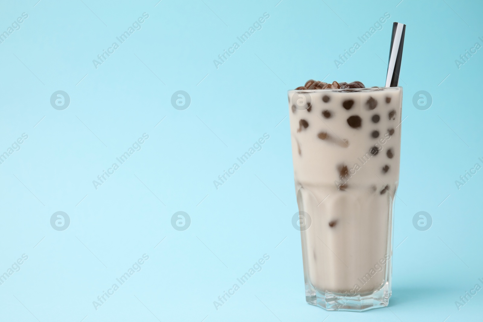 Photo of Tasty milk bubble tea in glass on light blue background, space for text