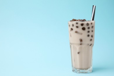 Photo of Tasty milk bubble tea in glass on light blue background, space for text