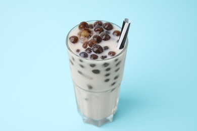 Photo of Tasty milk bubble tea in glass on light blue background, closeup