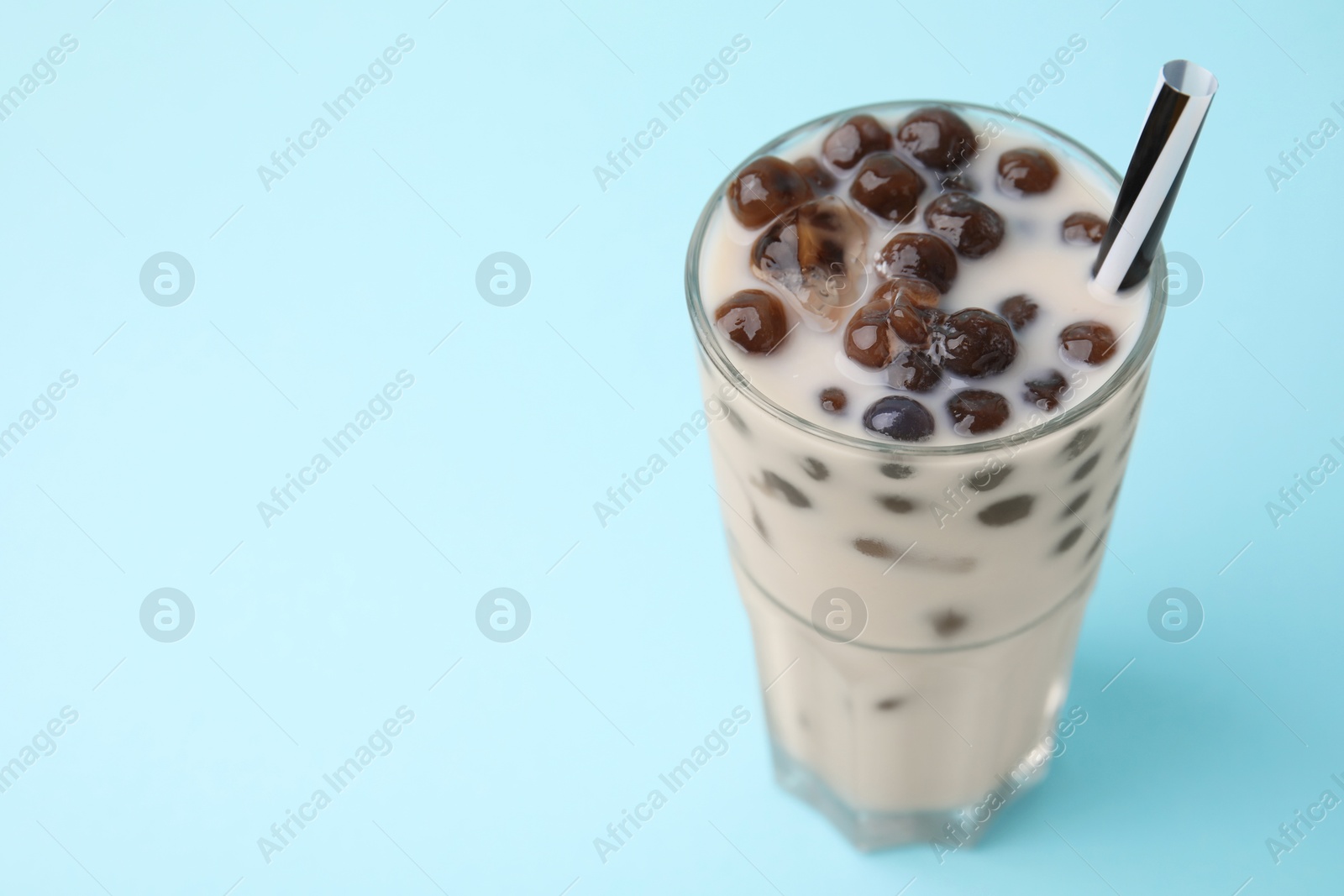 Photo of Tasty milk bubble tea in glass on light blue background, closeup. Space for text