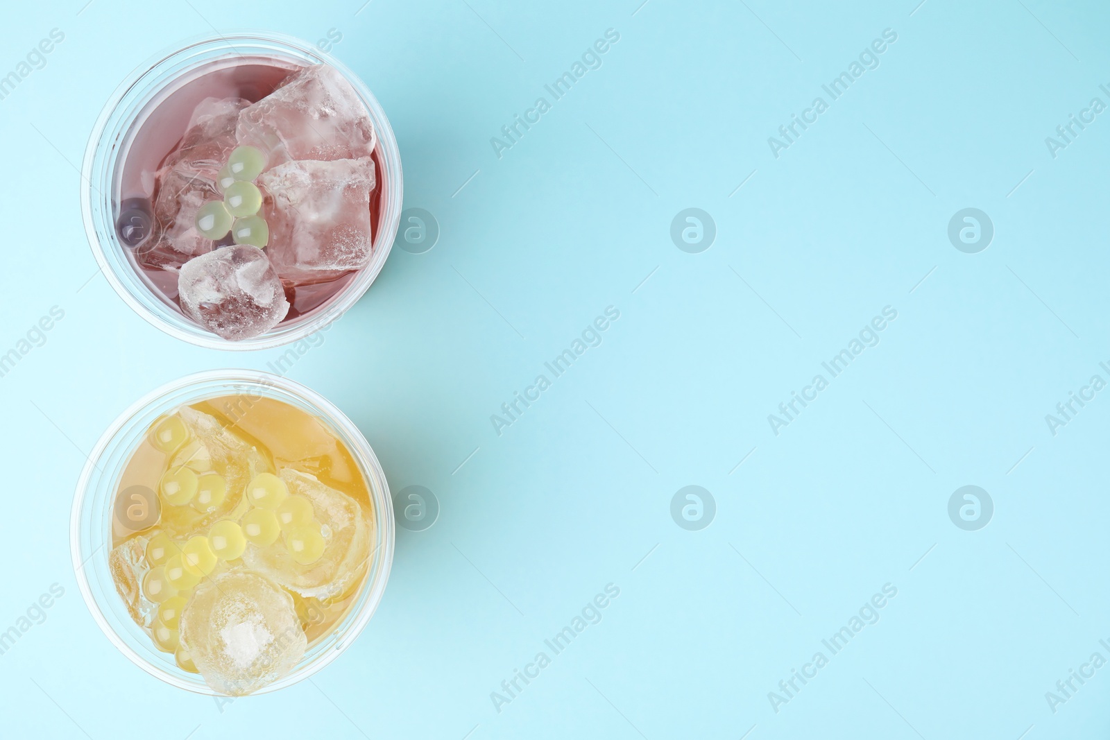 Photo of Tasty bubble tea in plastic cups on light blue background, flat lay. Space for text