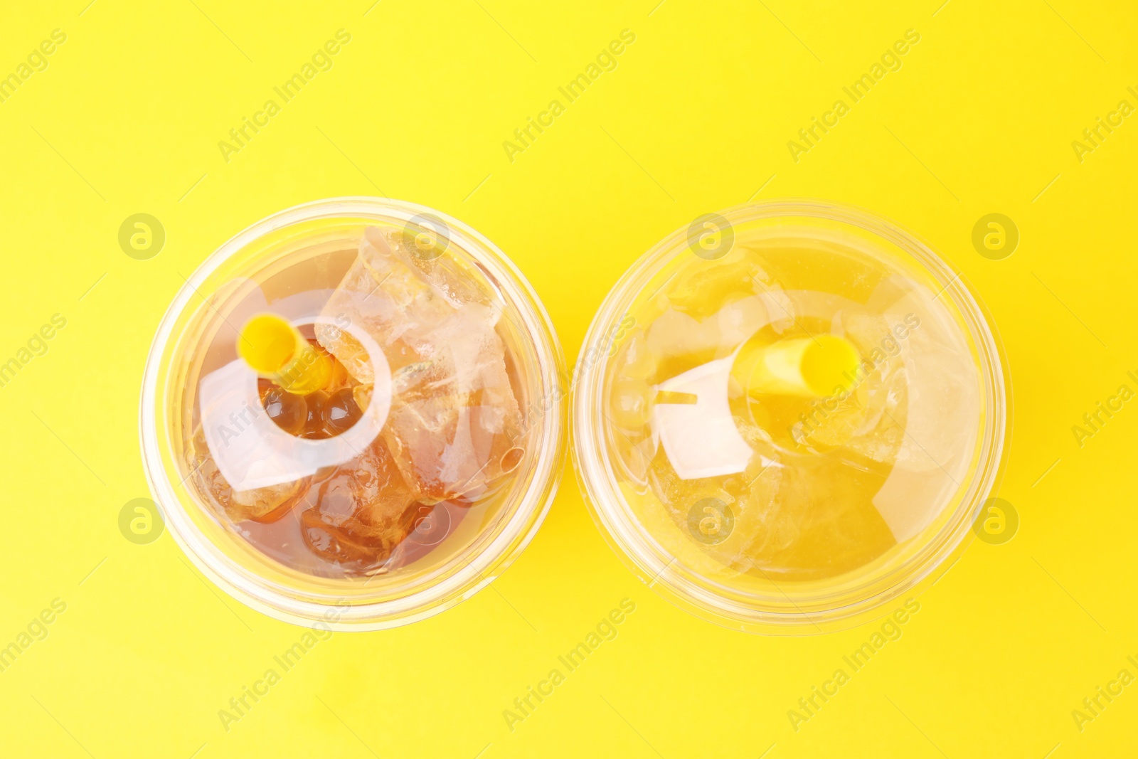 Photo of Tasty bubble tea in plastic cups on yellow background, flat lay