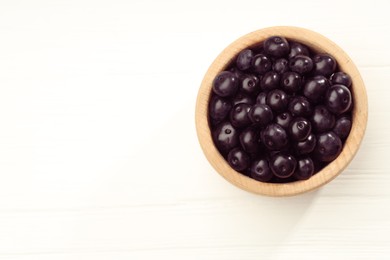 Ripe acai berries in bowl on white wooden table, top view. Space for text