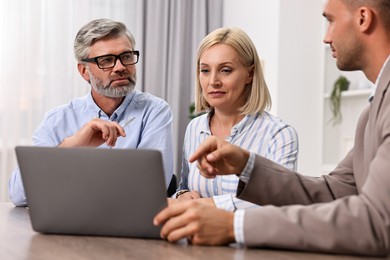 Pension plan. Couple consulting with insurance agent at table indoors