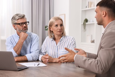 Photo of Pension plan. Couple consulting with insurance agent at table indoors